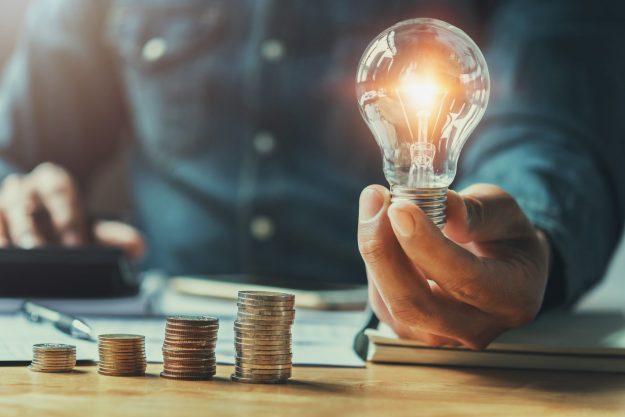 Business,Man,Hand,Holding,Lightbulb,With,Using,Calculator,To,Calculate reduce your energy costs